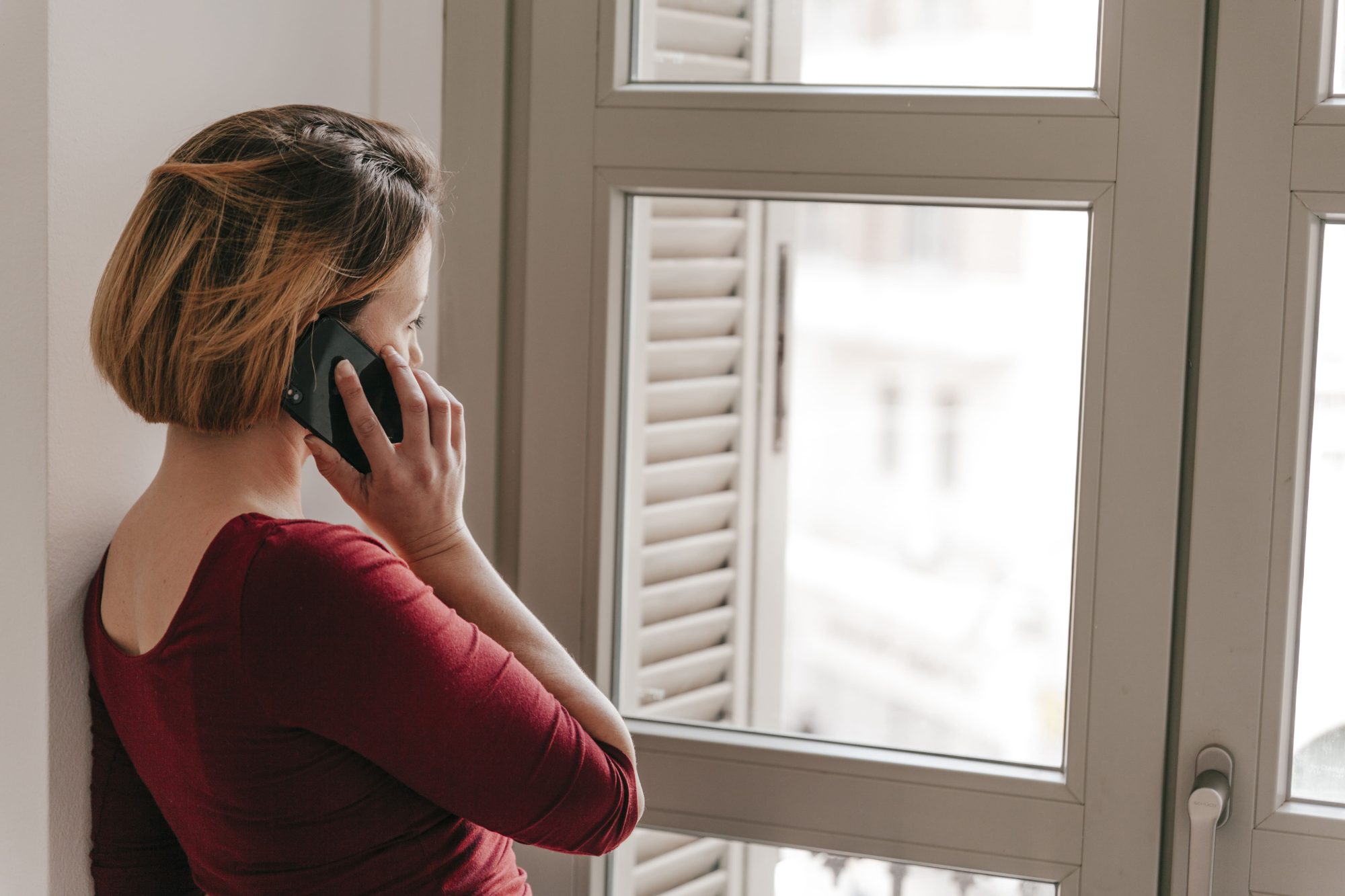 Mujer mirando a través de una ventana con vidrio bajo emisivo, iluminada por luz natural en un entorno cálido y confortable en una vivienda de Extremadura.